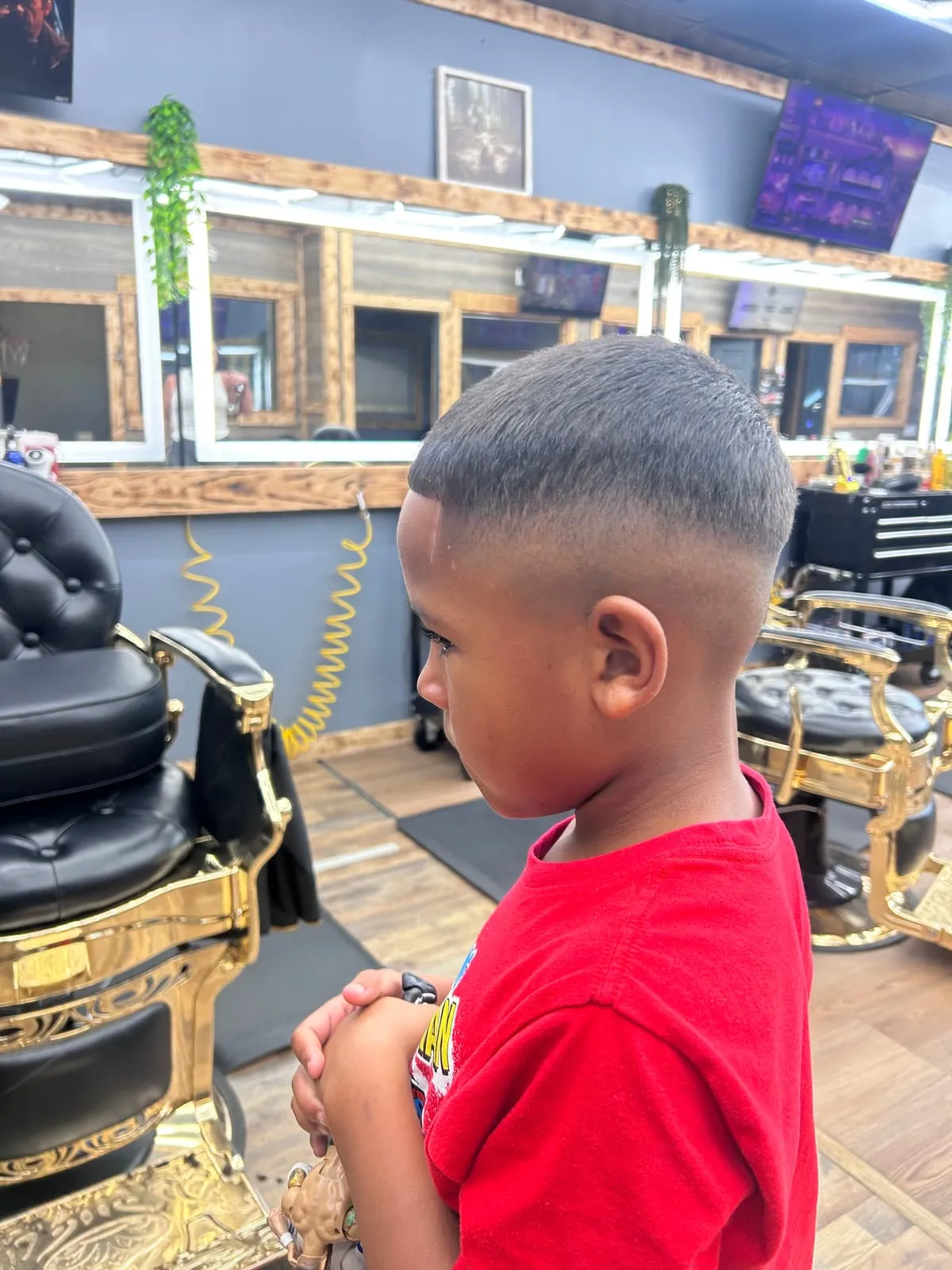 Boy in a red shirt, seen from the side, with a short top and a clean high fade
