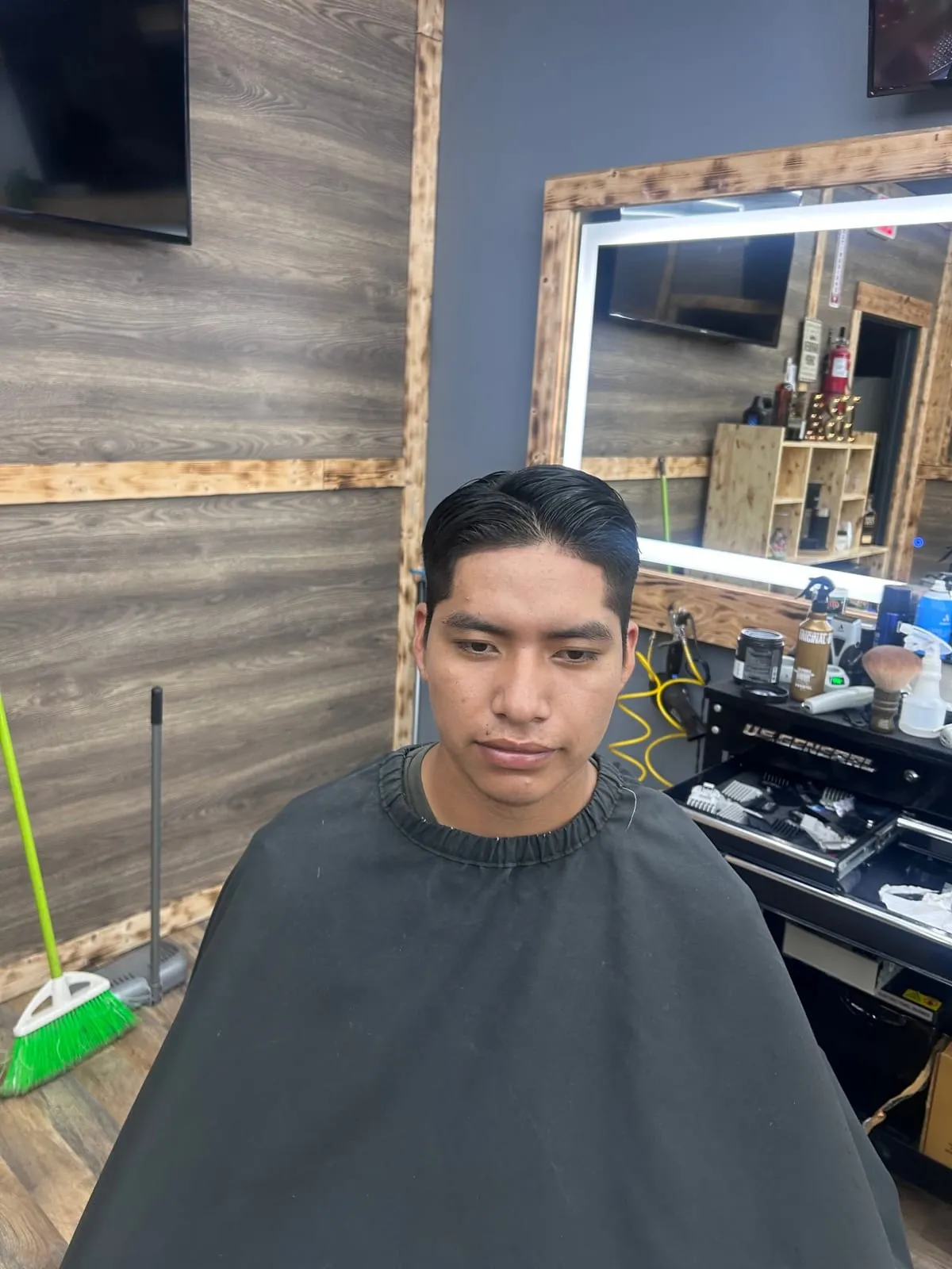 Man in a black cape with a smooth side-parted slick-back top and a tapered side
