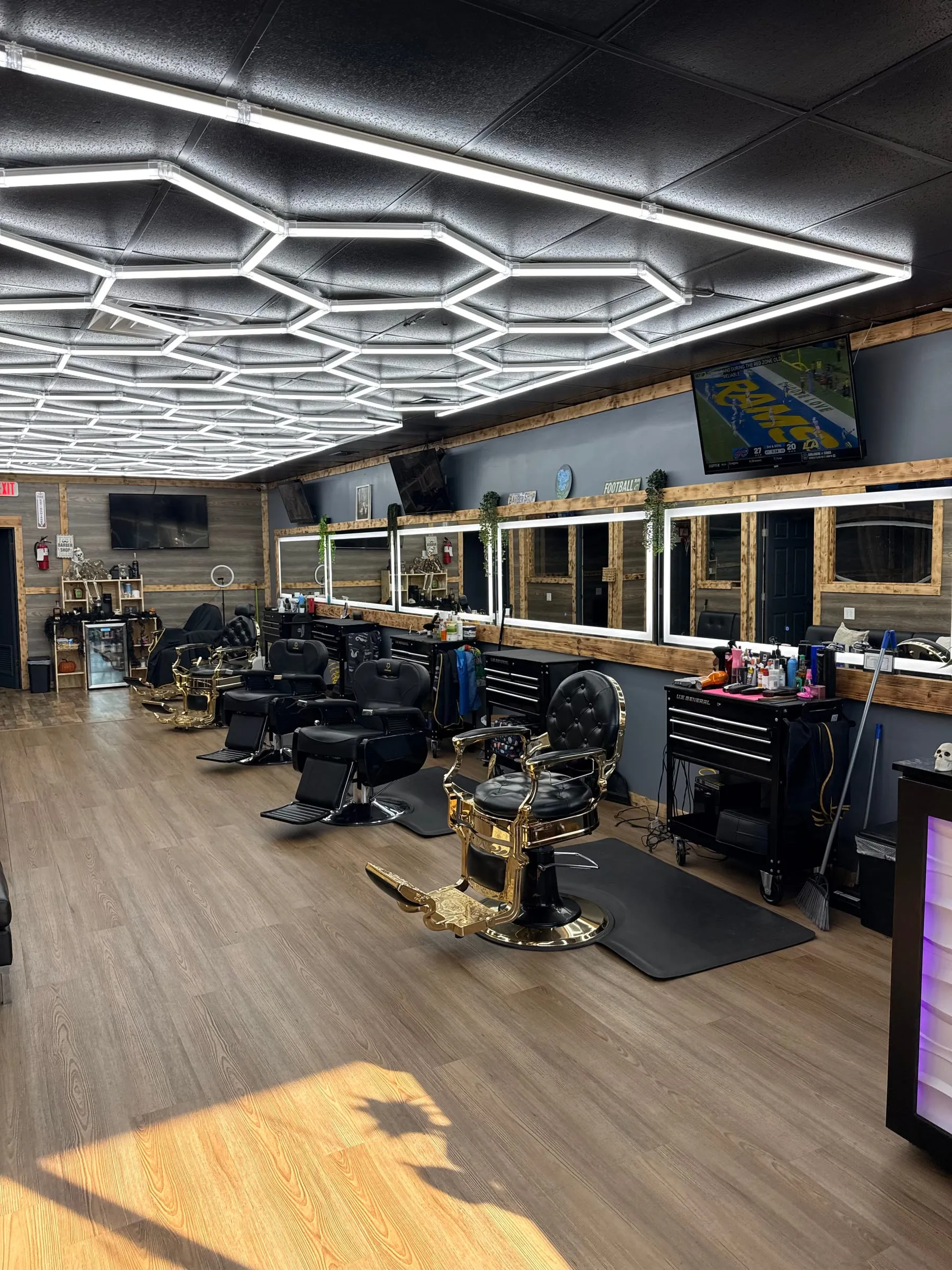 A row of black-and-gold barber chairs facing wood-framed mirrors under the hexagon ceiling lights at Taylor'D Cutz.