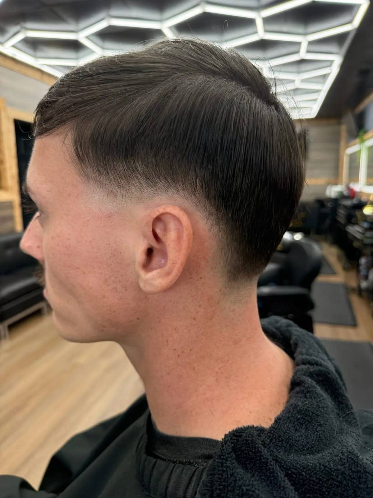Man seen from the side with a short, combed-forward top and a clean skin fade at the temple and neck
