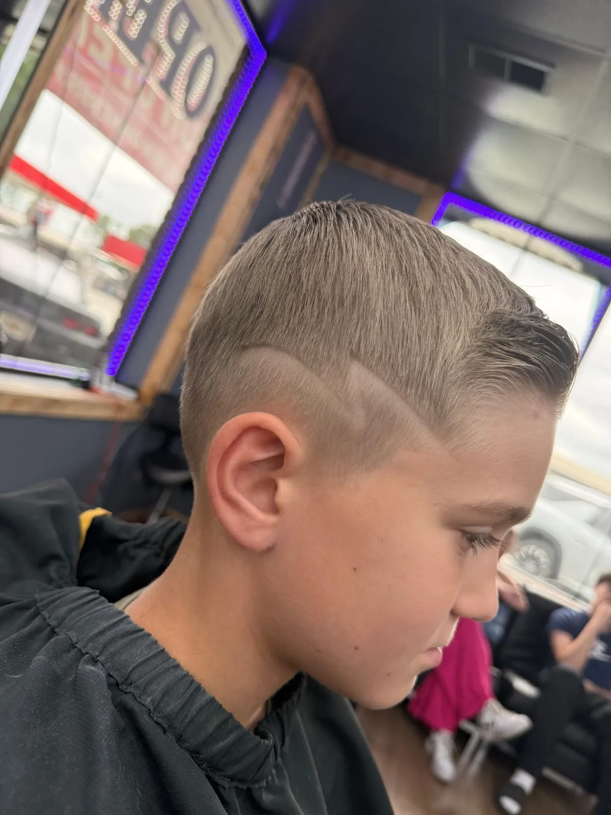 Boy looking down with a short side part and a razor-lined design shaved above the ear