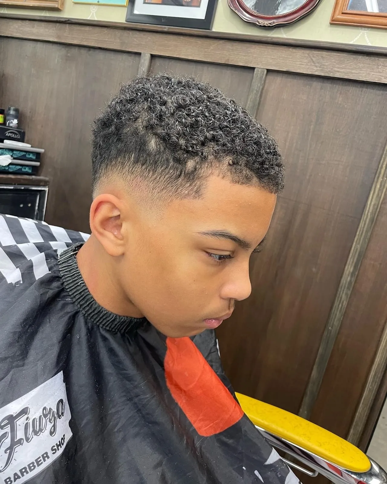 Boy looking down in a black cape with a curly top and a smooth fade on the sides